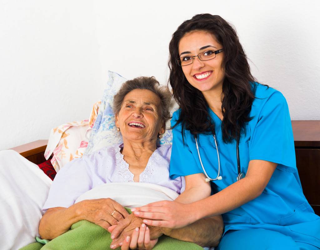 a nurse holding senior's hand while she is laying on bed