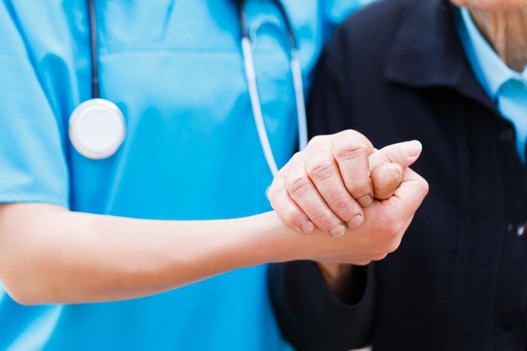 A nurse holding a senior's hand