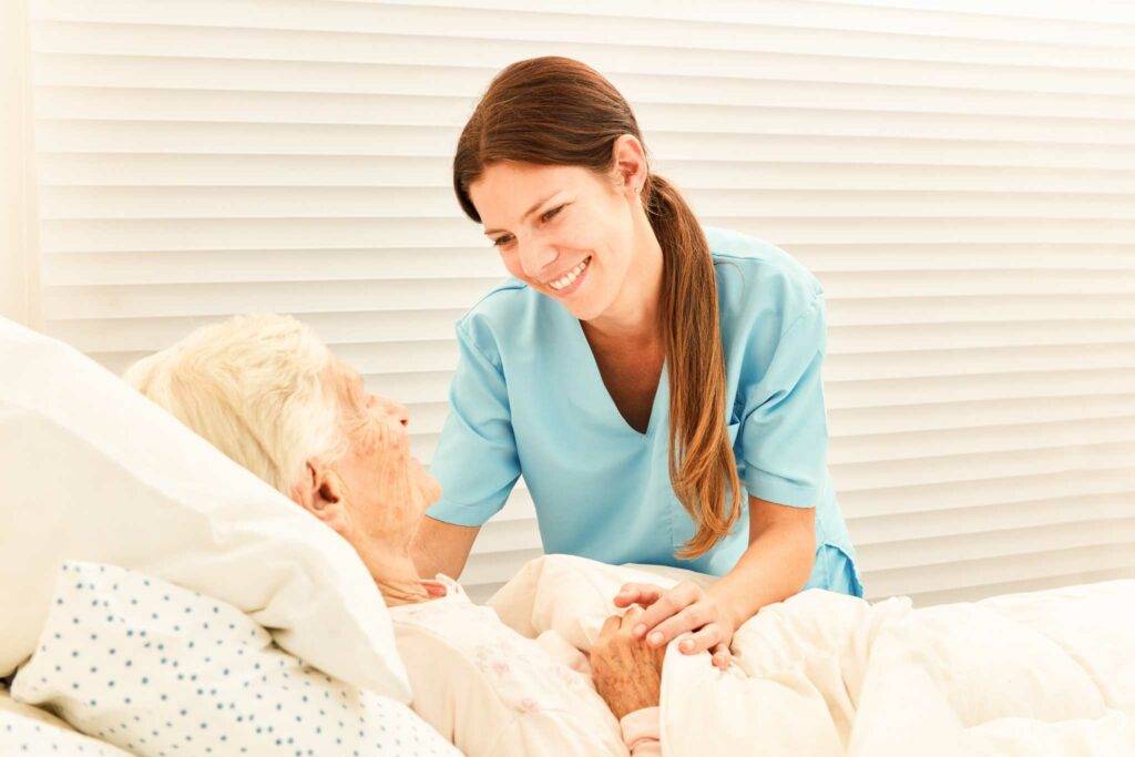 smiling female caregiver comforting an elderly lady laying in bed