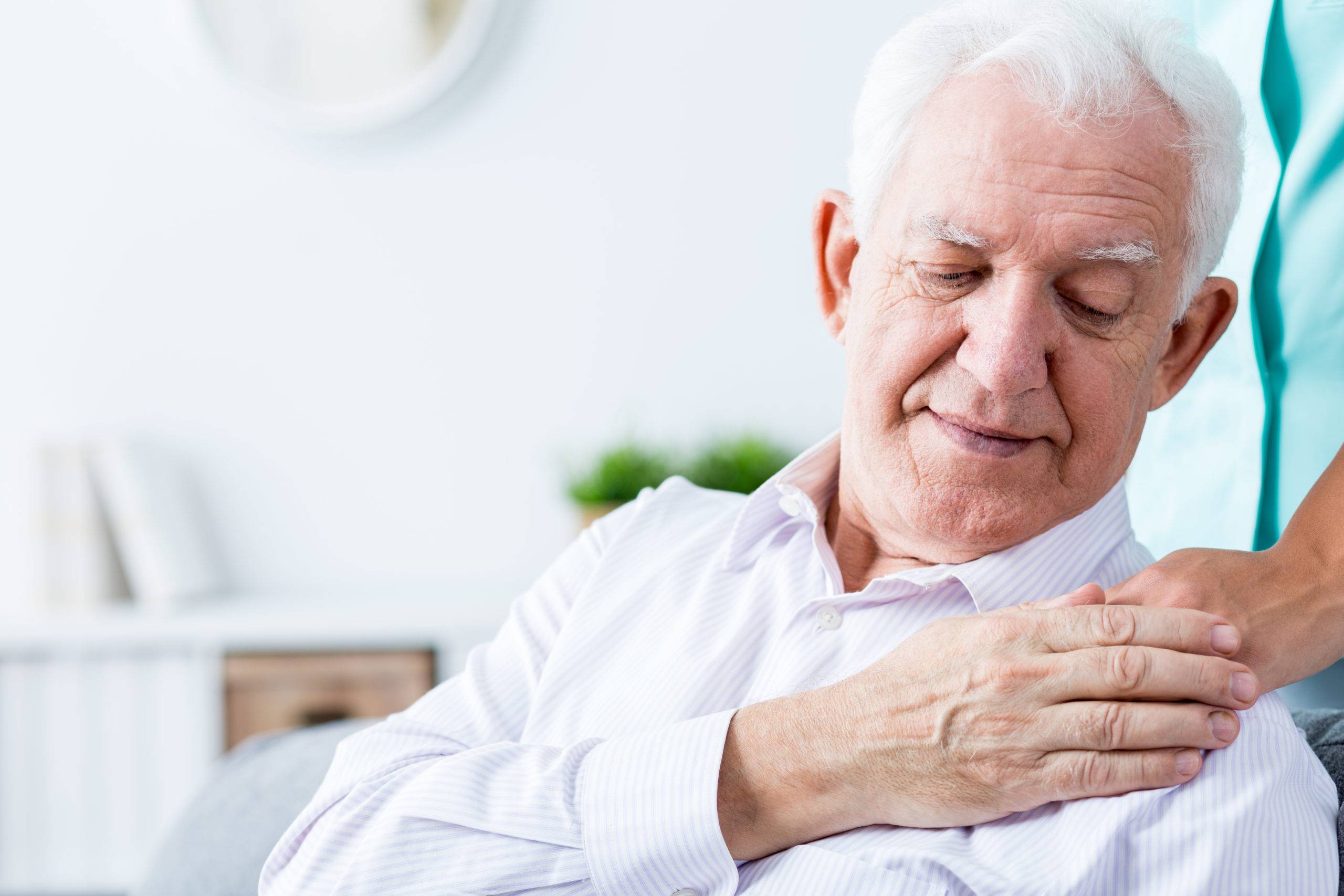 Senior man touching caregiver's hand on his shoulder.