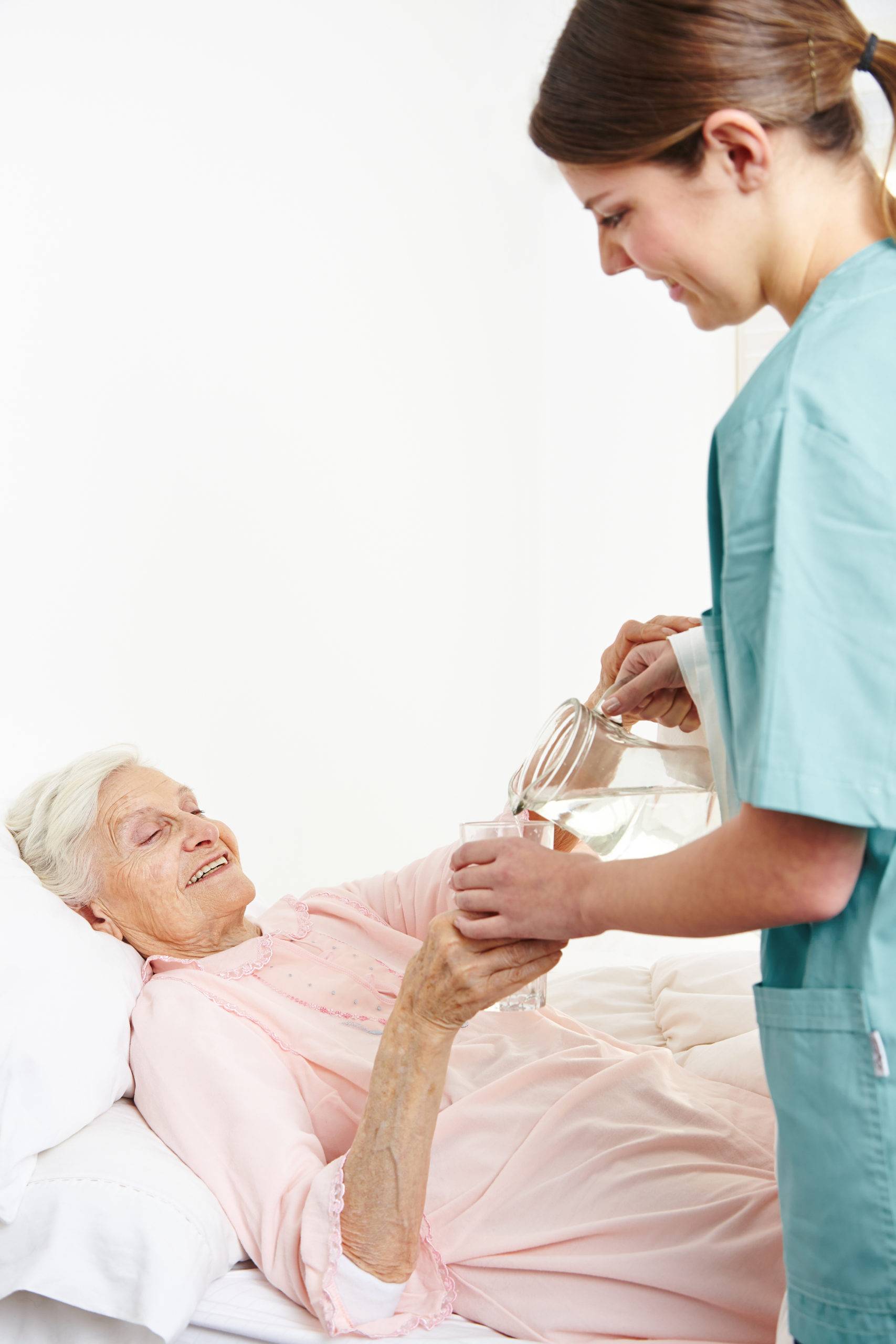 a nurse pouring glass of water for an elderly woman laying in bed